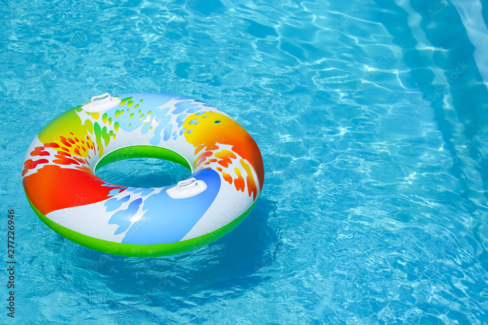 Colorful inflatable ring floating in swimming pool on sunny day. Space for text