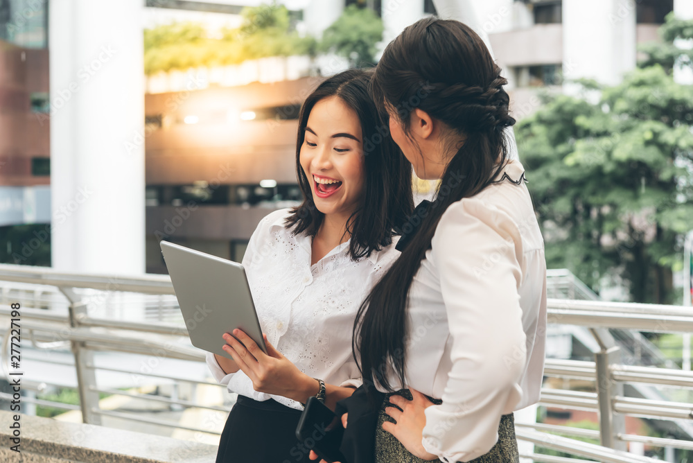 Pretty Asian women are smiling and happy while using genuine tablets, To view performance data During break time, to business concept. Pretty Asian women are smiling and happy while using genuine tablets, To view performance data During break time, to business concept.