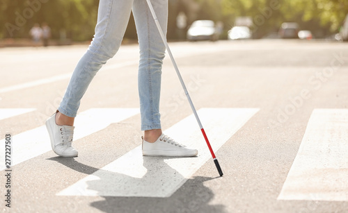 Blind person with long cane crossing road, closeup