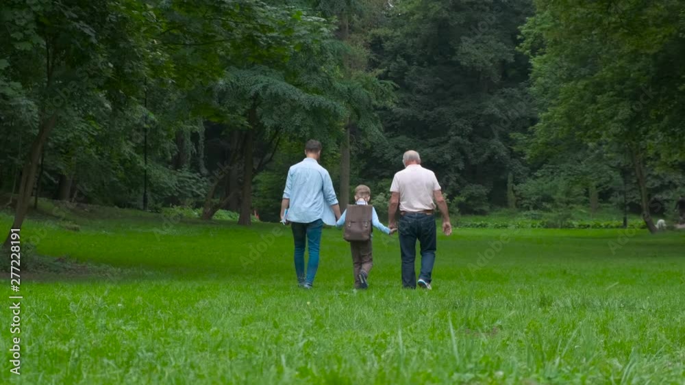 Family Generations concept: Father, son and Granddad, outdoors, in Nature, enjoying their Quality Time together, All in nice wear take child to school. Back view. Family Generations concept: Father, son and Granddad, outdoors, in Nature, enjoying their Quality Time together, All in nice wear take child to school. Back view.