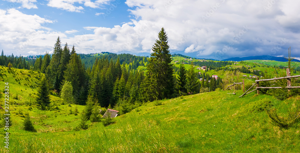 Picturesque spring Carpathians landscape panorama with an old hut in the forest and wooden split rail fence across a green and lush pasture on the valleys of Yablunytsya village, Ukraine
