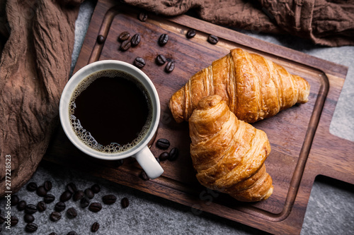 Fotografija Breakfast with fresh croissants and cup of black coffee on wooden board
