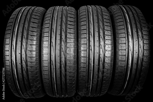 Studio shot of a set of summer car tires isolated on black background. Tire stack background. Car tyre protector close up. Black rubber tire. Brand new car tires. Close up tyre profile. Tires in a row