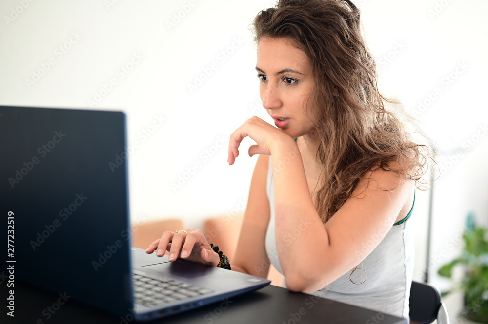Cute girl surprised by something while working at home from behind her laptop Cute girl surprised by something while working at home from behind her laptop