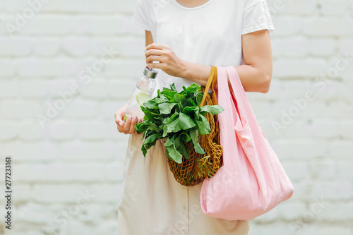 Female hands hold eco bag of vegetables, greens and reusable water bottle. Zero waste. Sustainable lifestyle concept. photo