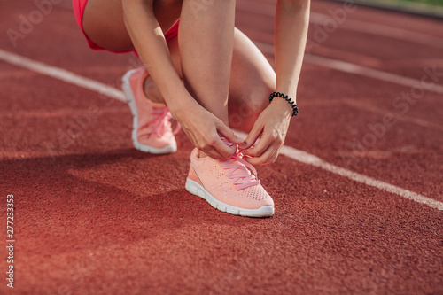 Young woman hands tie laces on her pink sport shoes on a stadium on a running path. White stripe near her. Close-up of tying shoes photo