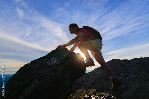 Silhouette of young woman climbing a rock.