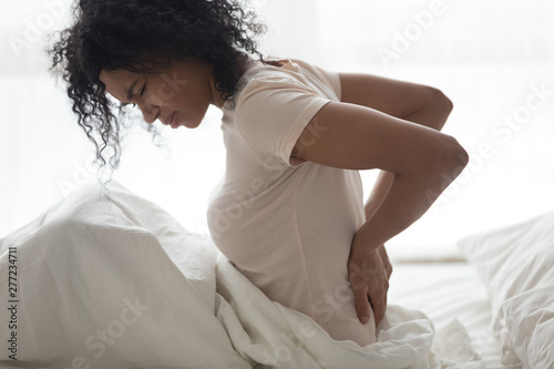 Sad young african woman touching back feeling backache in bed photo