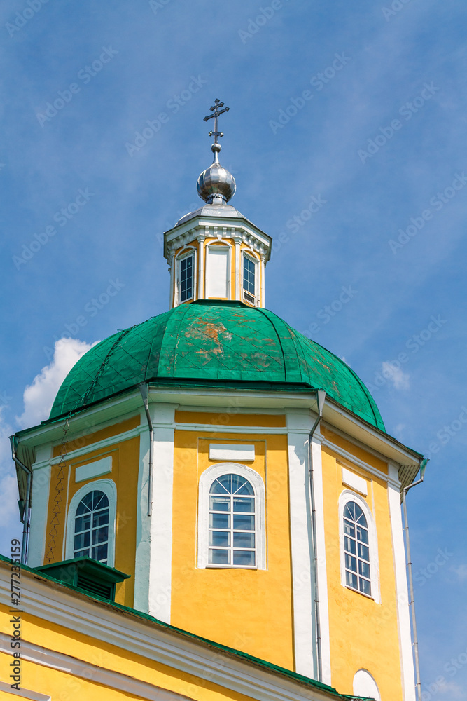 Yellow Orthodox Christian church with a green dome in summer against a blue sky with white clouds.