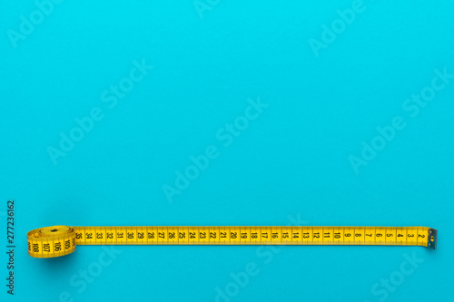 Top view of yellow soft measuring tape. Minimalist flat lay image of tape measure with metric scale over turquoise blue background with copy space. Photo of body measuring tape as diet concept.
