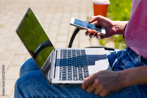 Woman using multiple devices phone laptop and tablet lying in a wood bench in a park