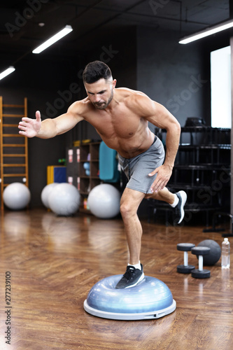 Fit athlete performing exercise on gymnastic hemisphere bosu ball in gym. photo