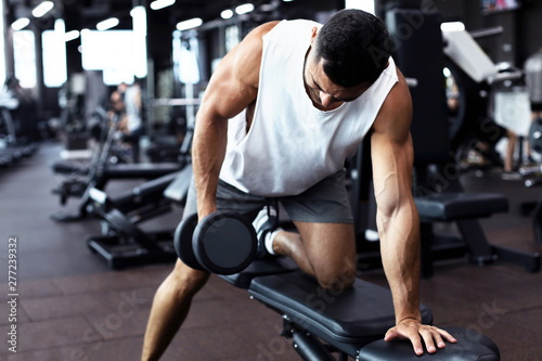 Fit and muscular man trains with dumbbells.