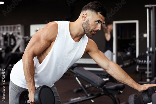 Fit and muscular man trains with dumbbells.