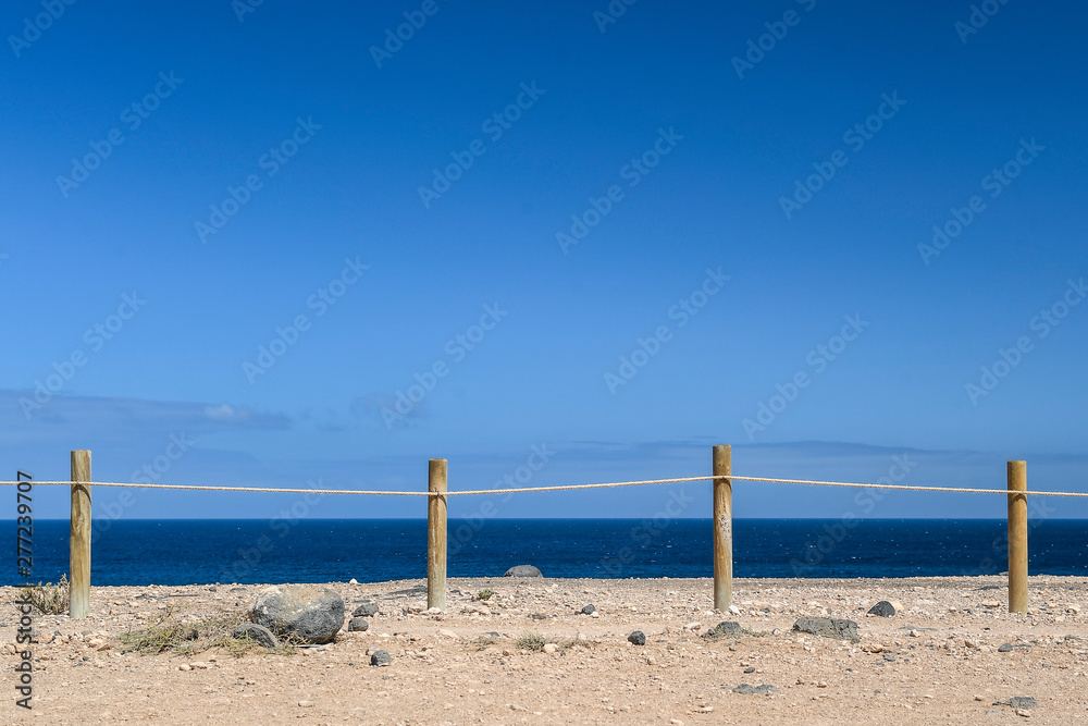 Natural marine landscape with amazing blue water near El Coralejo Fuerteventura Canary Island Spain. Summer exotic vacation postcard from a tropical island in the ocean. Row of wooden posts with rope.