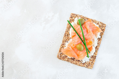 Sandwich with smoked salmon and cream cheese on thin multi seed  crispbread, garnished with green onion and olives, horizontal, top view, copy space