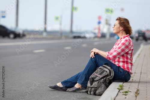 Mature woman hitchhiker sitting on roadside and waiting the car