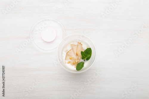 Yogurt pear slices and mint and pine nuts lie in a lunch box on a white table next to scattered with pine nuts and pear slices. Healthy eating concept. Copy space