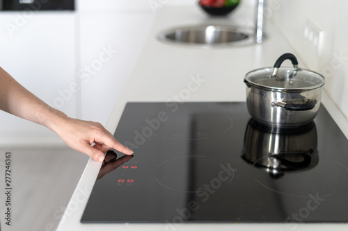 Woman using built in stove with saucepan on top, selecting program on display