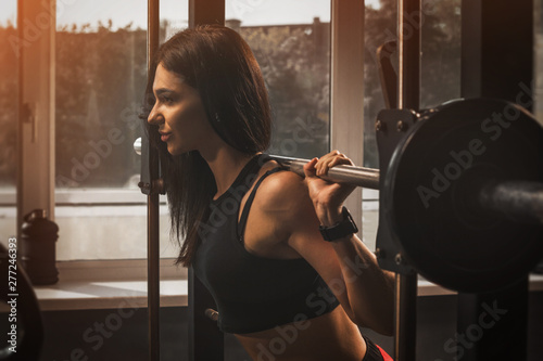 Young fit athletic girl having workout in gym. Brunette beautiful healthy female indoor training.