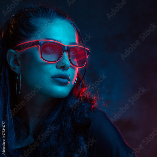 Sensual woman in neon glasses portrait. Beautiful younG female model iwearing oink neon glasses iisoalted in red light over concete wall background photo