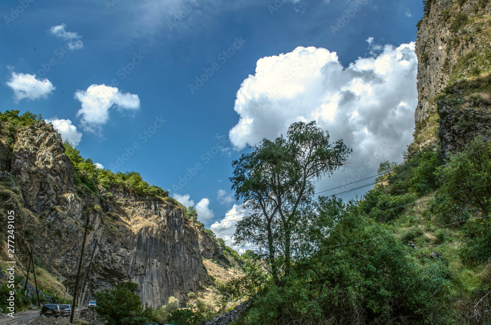 Mountain road to Garni gorge near vertically standing basalt rocks and hills on the background of blue sky covered with clouds  