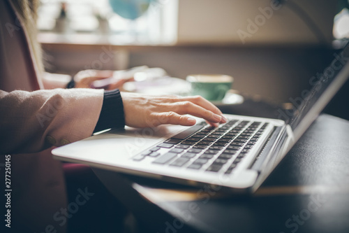 Close-up top view of Caucasian woman's hands Casually dressed student, blogger, writer man working on a laptop holding a phone in his hand, inside the cafe a wooden table and a cup of coffee