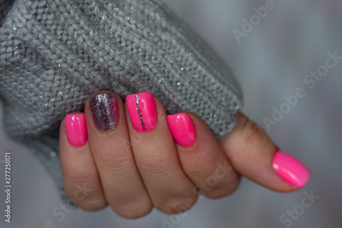 The pink manicure with the knitted sleeve of a grey sweater on grey background. Winter concept.