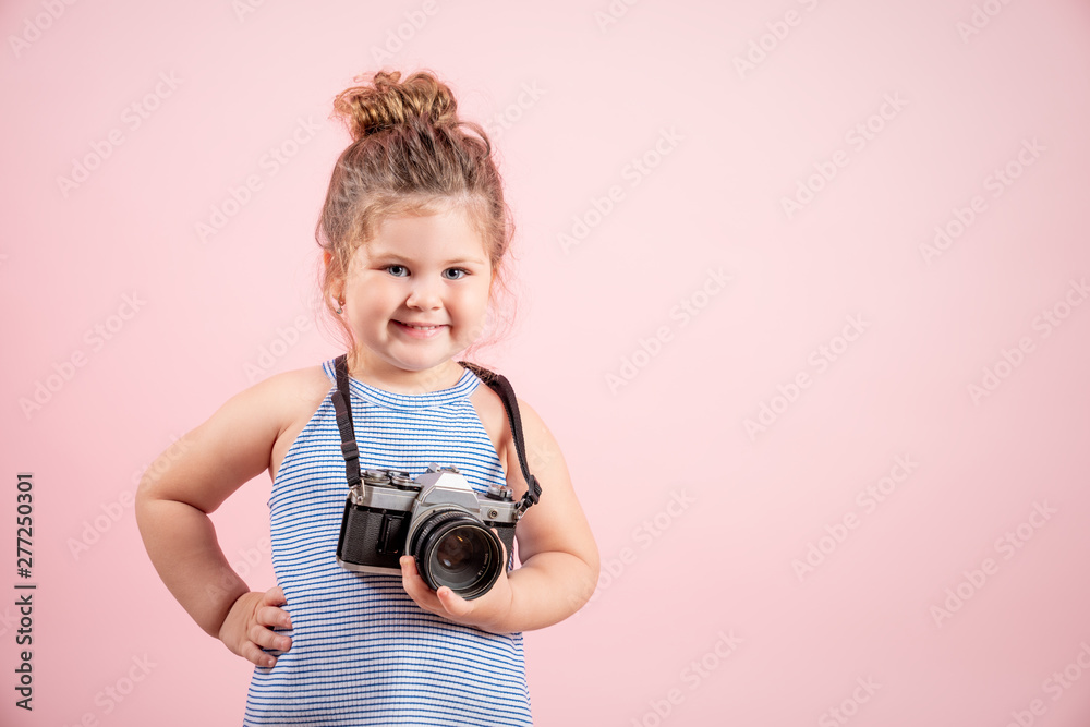 Fototapeta premium Little girl holding old vintage camera and smiling on pink background