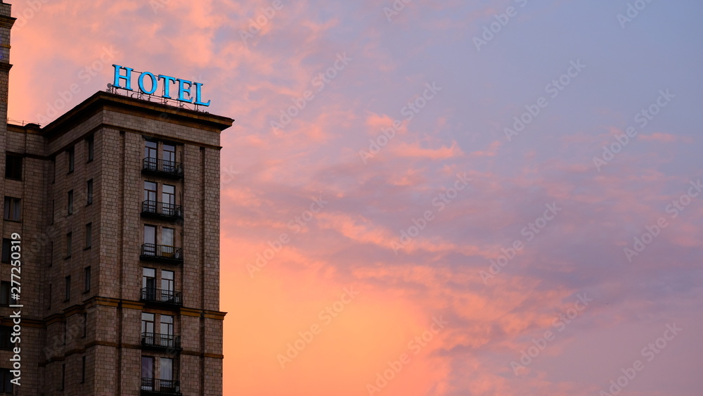 Weathered and burned out neon hotel sign lit up against a colorful and dramatic red and orange sky at sunset in New York