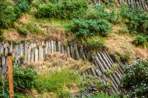 Rock with slope and natural terraces supported by basalt columns, covered with flowering shrubs and grass in Garni gorge in Armenia