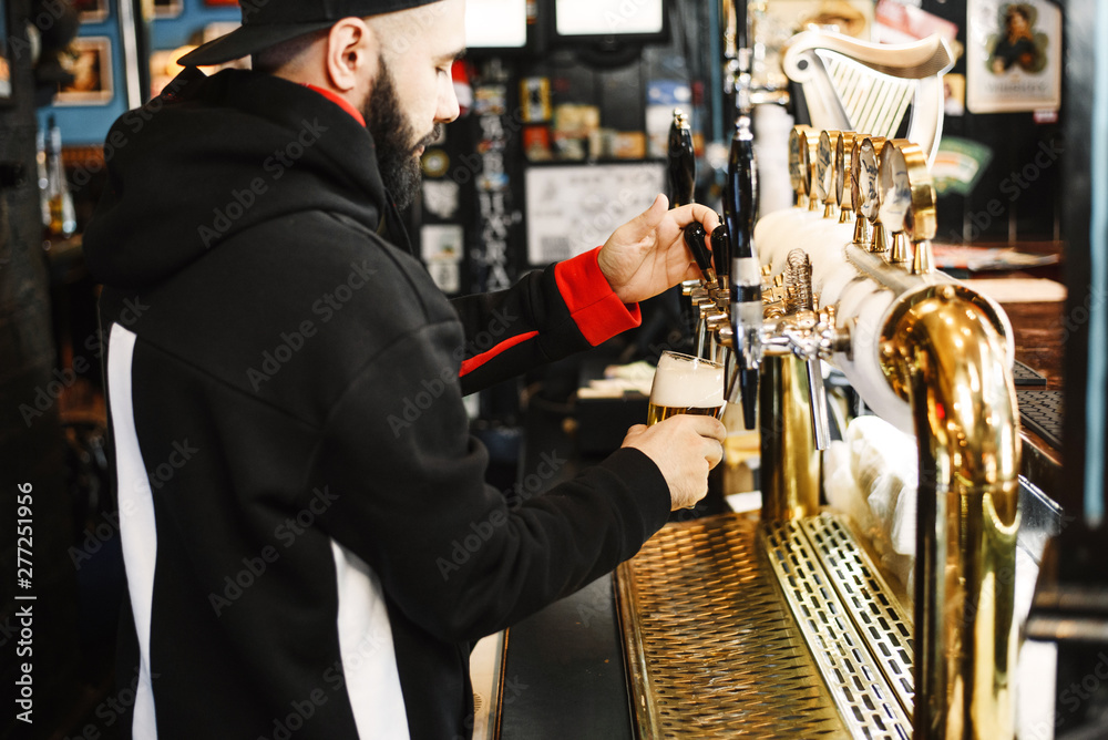 smiling barman pouring beer in a bar. Bearded courageous man pours you a foaming drink. Golden tap for draft beer