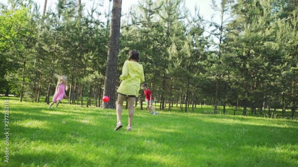 Group of three children playing dodgeball game on green grass in summer park. Girl throwing ball trying to hit friends in slow motion Group of three children playing dodgeball game on green grass in summer park. Girl throwing ball trying to hit friends in slow motion
