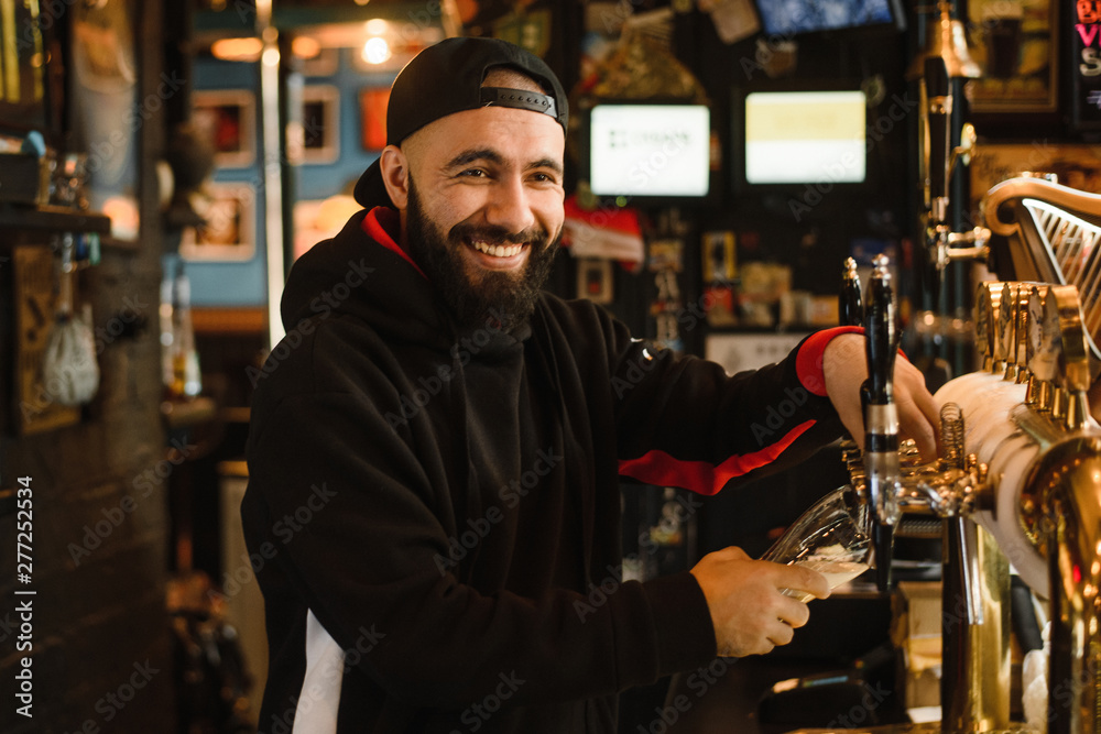 smiling barman pouring beer in a bar. Bearded courageous man pours you a foaming drink. Golden tap for draft beer