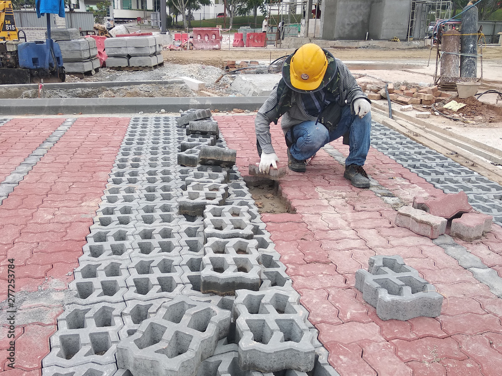 Concrete pavers preparation and installation work by workers at the construction site car park area. It is arranged following the pattern and approved colour.  
