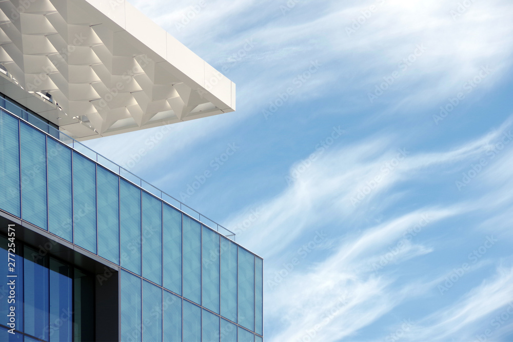 View of the top corner of a city building with a modern lass facade and blue sky and vivid clouds behind