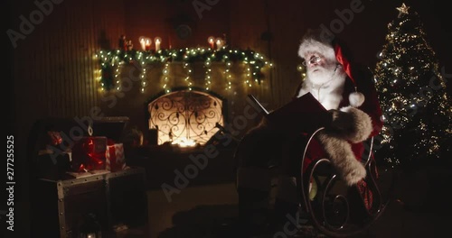 Santa claus sitting on roker in specially decorated room, reading a magical shining book - holidays and celebrations, christmas spirit concept 4k footage photo