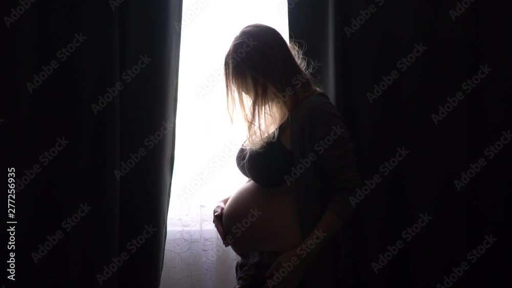 pregnant girl stroking her belly and smile. Woman in gray bathrobe pregnant girl stroking her belly and smile. Woman in gray bathrobe