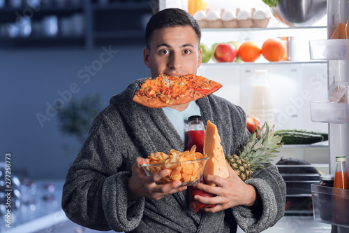Afraid man caught in the act of choosing tasty food near refrigerator at night photo