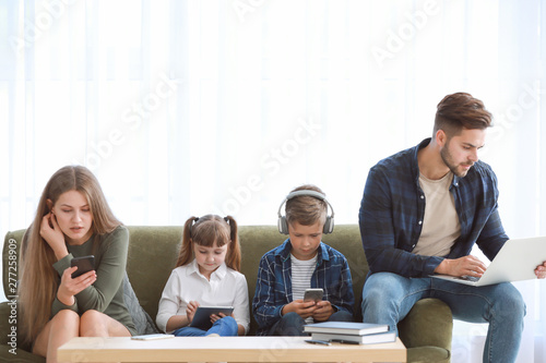 Family addicted to modern technologies with devices sitting on sofa at home