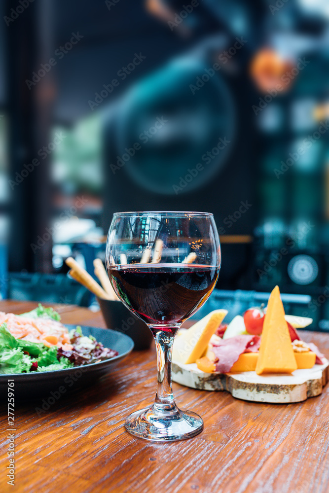 Dinner in the restaurant with Wine, Cheese and salad. Red wine glass, assorted cheese plate and smoked salmon salad on wooden dining table. This is Lunch or Dinner Restaurant or Cafe Concept Image.