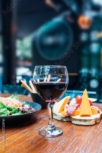 Dinner in the restaurant with Wine  Cheese and salad. Red wine glass  assorted cheese plate and smoked salmon salad on wooden dining table. This is Lunch or Dinner Restaurant or Cafe Concept Image.