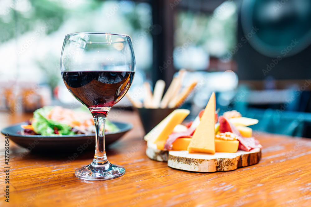 Dinner in the restaurant with Wine, Cheese and salad. Red wine glass, assorted cheese plate and smoked salmon salad on wooden dining table. This is Lunch or Dinner Restaurant or Cafe Concept Image. Dinner in the restaurant with Wine, Cheese and salad. Red wine glass, assorted cheese plate and smoked salmon salad on wooden dining table. This is Lunch or Dinner Restaurant or Cafe Concept Image.