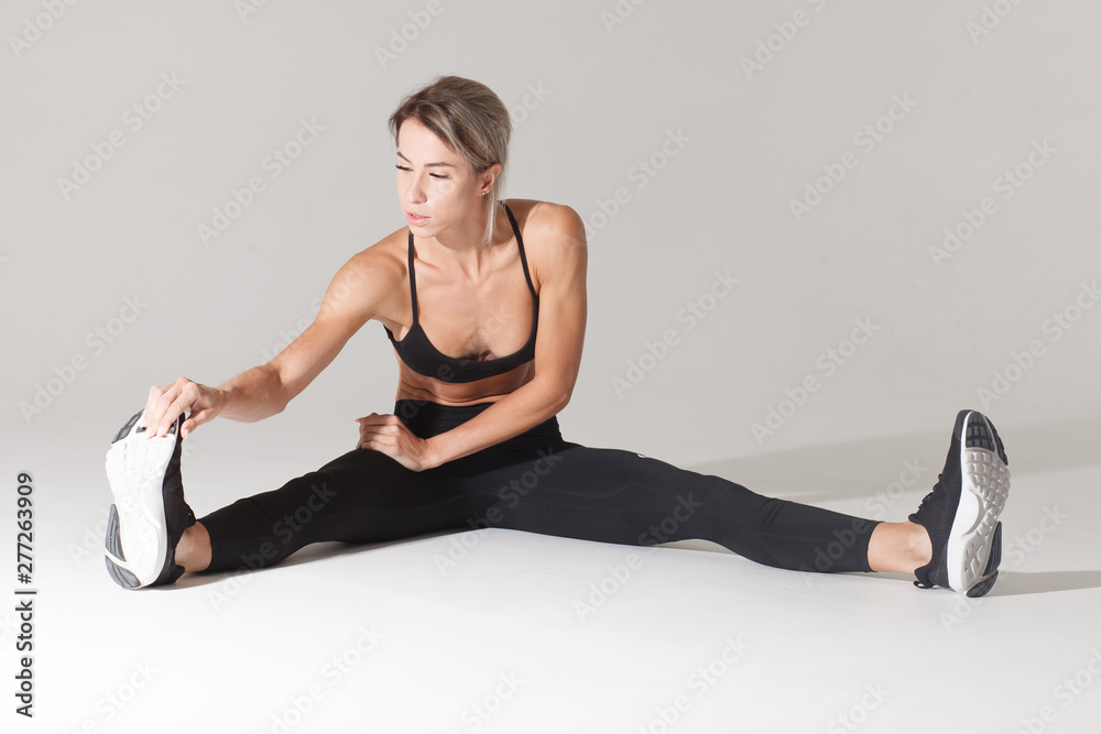 Obraz premium athletic blonde sportswoman stretching warming up legs isolated on white background with shadow