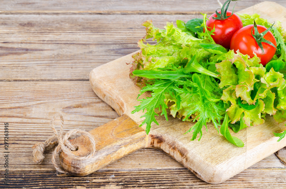 Green salad ingredients organic lettuce, cherry tomatoes, spices and olive oil on wooden background. 