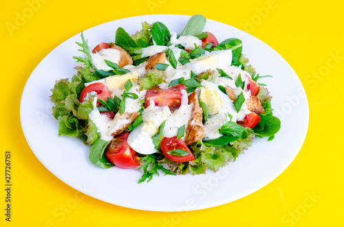 Salad of lettuce, egg, chicken pieces, mayonnaise on white plate on yellow background