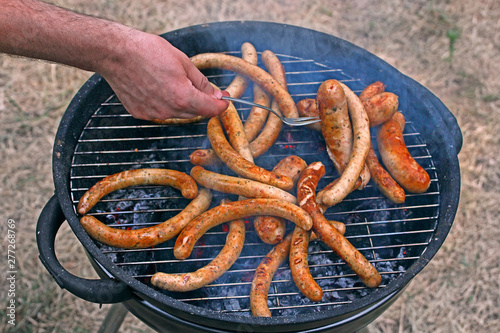 stir with a fork fried sausages and sausages on the grill in the smoke
