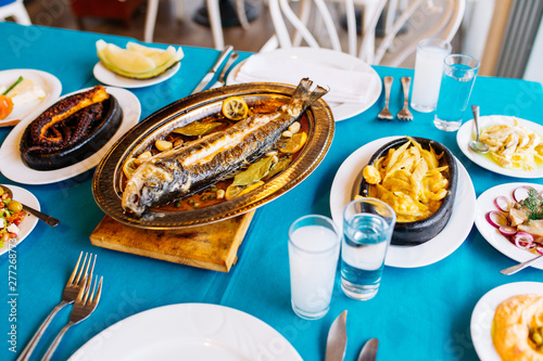 Turkish or Greek restaurant table and food dinner cuisine culture from top view. Traditional Greek ouzo or turkish raki with grilled or fried fish and appetizers on dinner table at restaurant.  photo