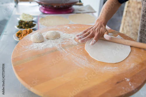 Woman preparing or making borek or bread dough. Hands keep rolling pin on dough with flour. Borek, bread or pastry dough on a wooden table background. Traditional Turkish pide, pita or yufka bread. photo