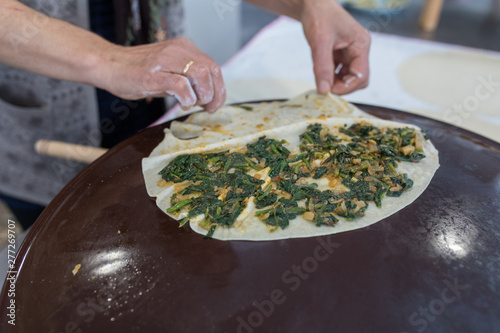 Woman preparing or making borek or bread dough. Hands keep rolling pin on dough with flour. Borek, bread or pastry dough on a wooden table background. Traditional Turkish pide, pita or yufka bread. photo